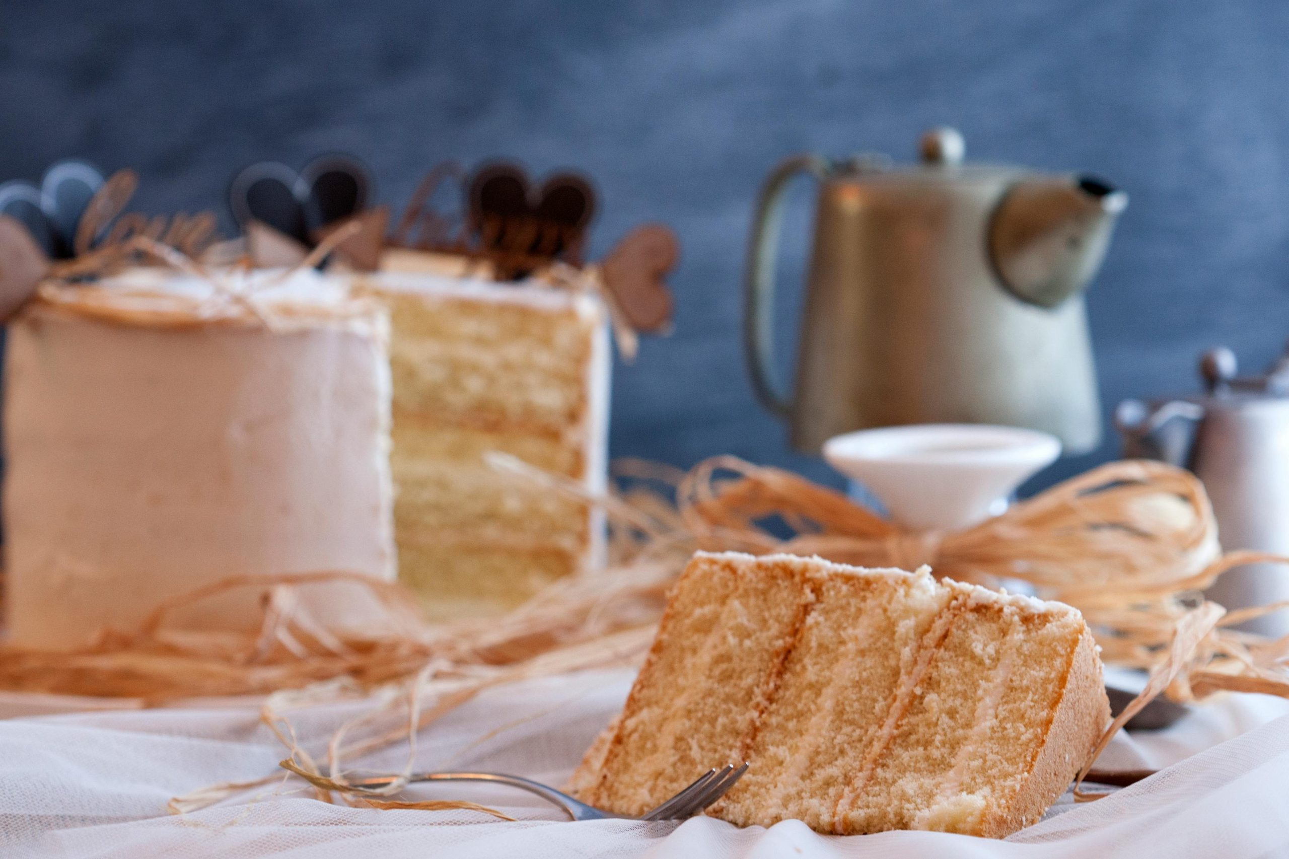 A delightful slice of layered cake with a vintage teapot in a cozy setting, perfect for indulgence.