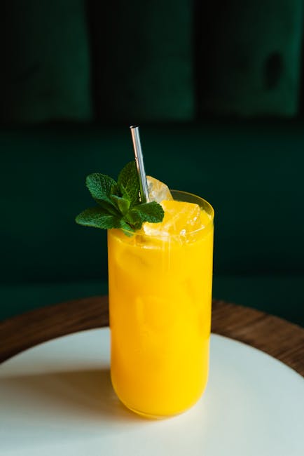 Bright citrus cocktail with ice and mint served on a wooden table in a sleek glass.
